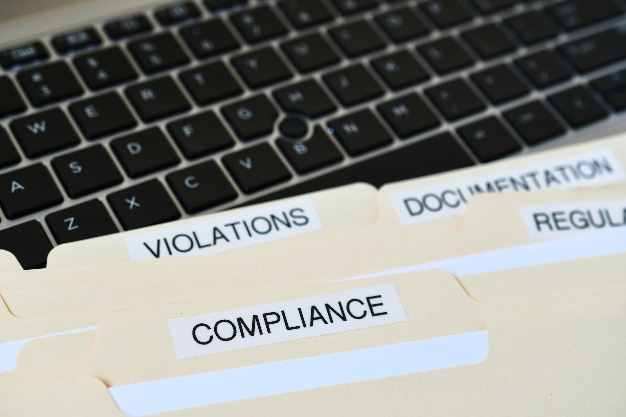 File Folders with words Compliance, Violations, Documentation on black computer keyboard